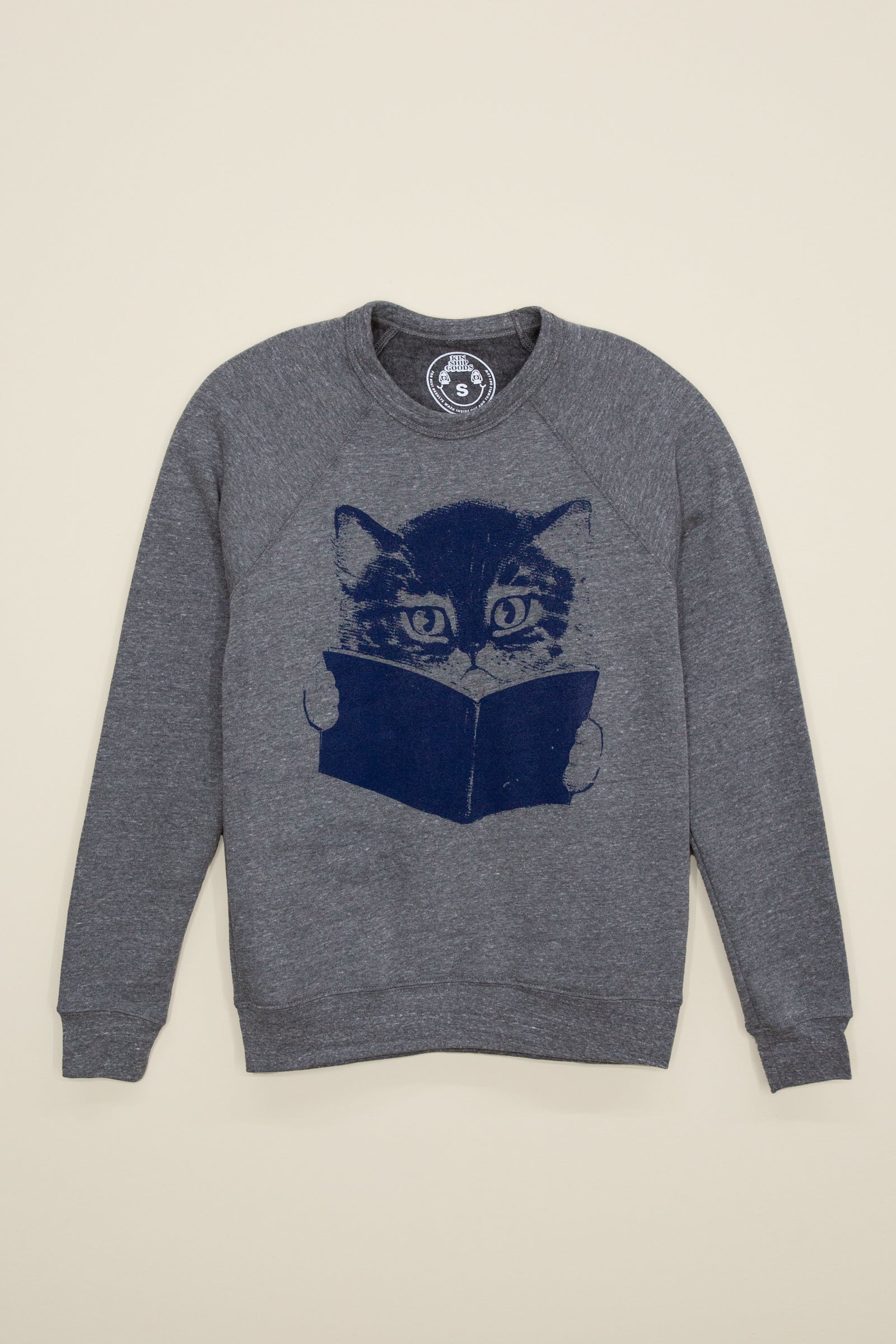 Gray Kin Ship Goods sweatshirt with navy graphic of a cat reading a book, laid flat on light background.