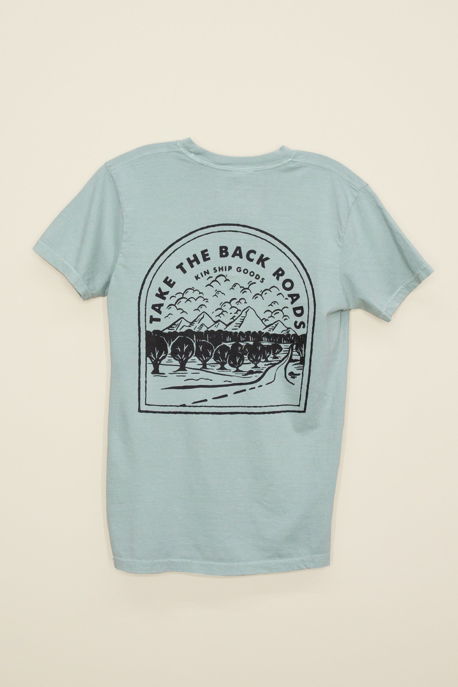Kin Ship Goods light blue/green pocket tee with ‘Take the Back Roads’ mountain and orchard graphic on back, perfect for slow travel and scenic drives.